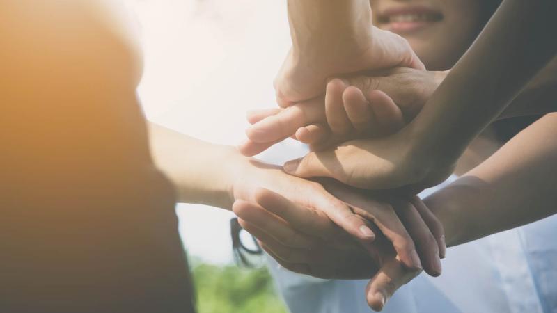 Stock image of people stacking their hands on top of each other's in solidarity.