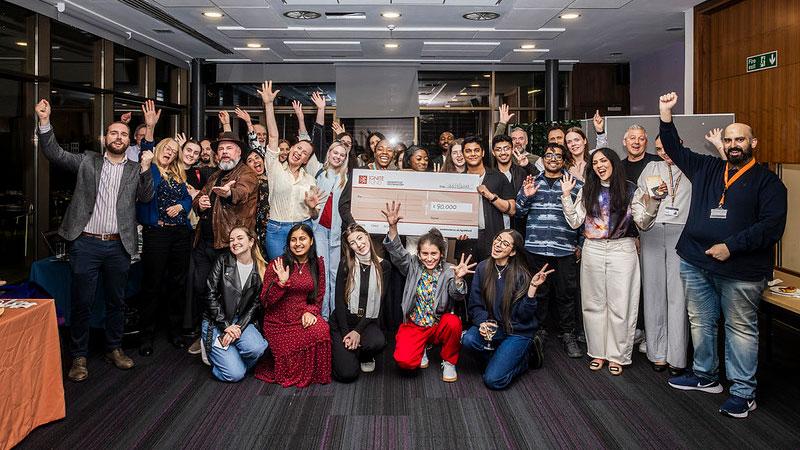 Group photo of attendees at the Ignite Fund celebration event. In the middle people are holding a large cardboard cheque.