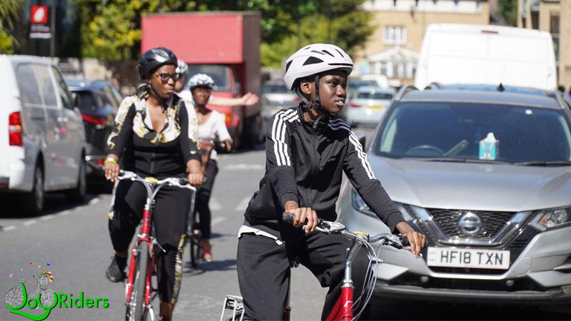 Photo of a child and two adult women riding bikes. In the bottom left corner there is the JoyRiders logo in green text.