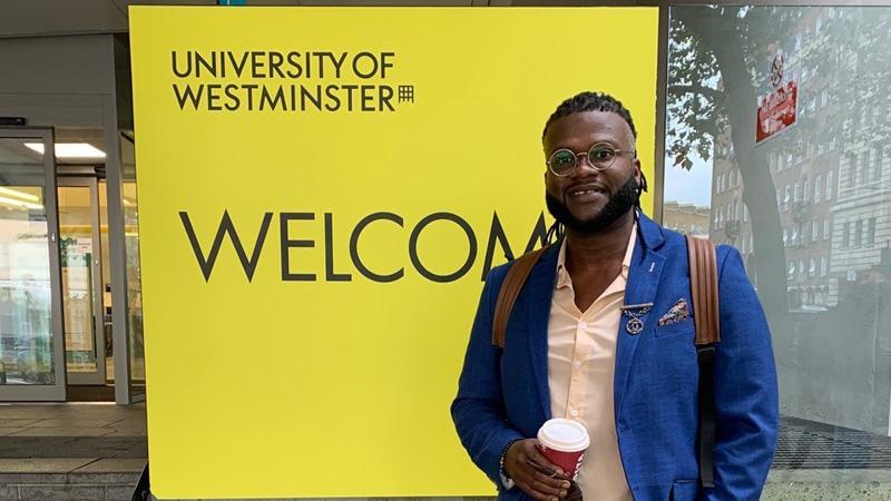 Student Lonceny Kourama stood in front of yellow University of Westminster WELCOME sign