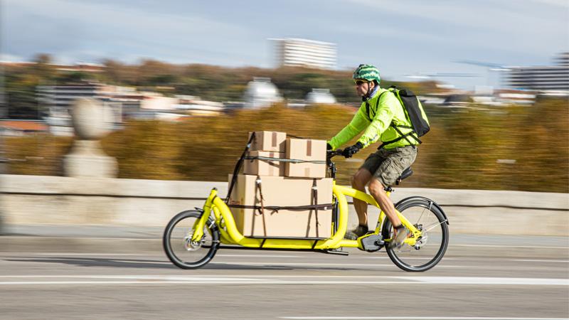 Man riding cargo bike on road with cardboard boxes attached