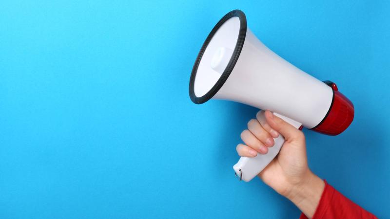 Picture of hand holding a megaphone in front of blue background.