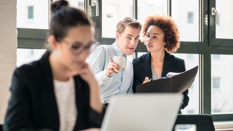 Stock image of office workers gossiping behind another colleague's back.