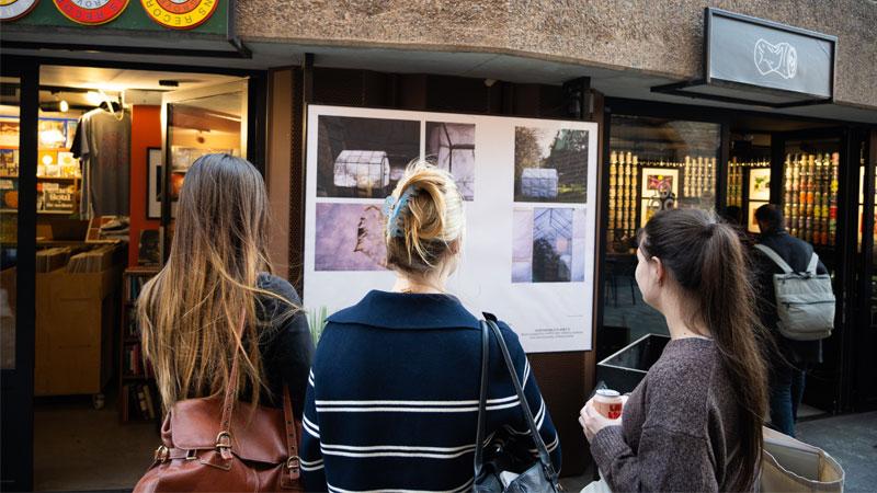 The backs of three people's heads as they view student artwork in the Earth Day exhibition.