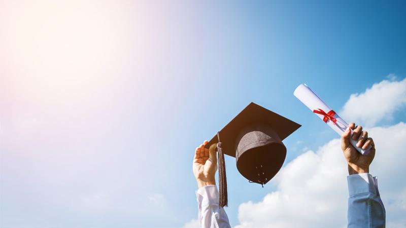 Person holding up a graduation cap and scroll in each hand on a sky background