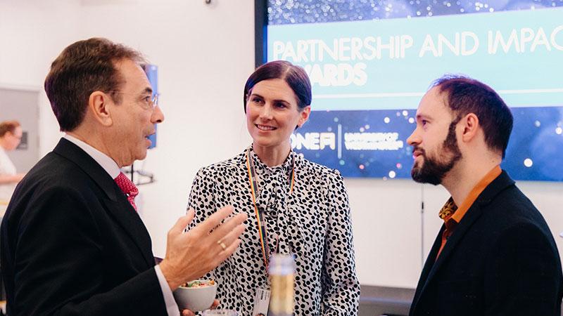 A group of people talking in front of a screen that says PARTNERSHIP AND IMPACT AWARDS