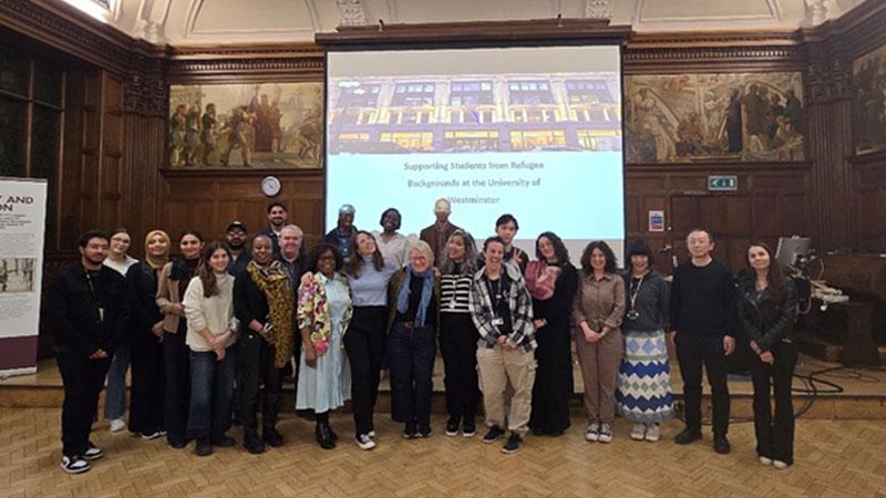 A group photo of attendees smiling in front of a projector which reads: Supporting Students from Refugee Backgrounds at the University of Westminster