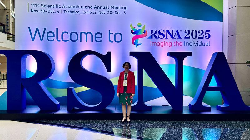 Louise Thomas standing by a large sign that reads Welcome to RSNA