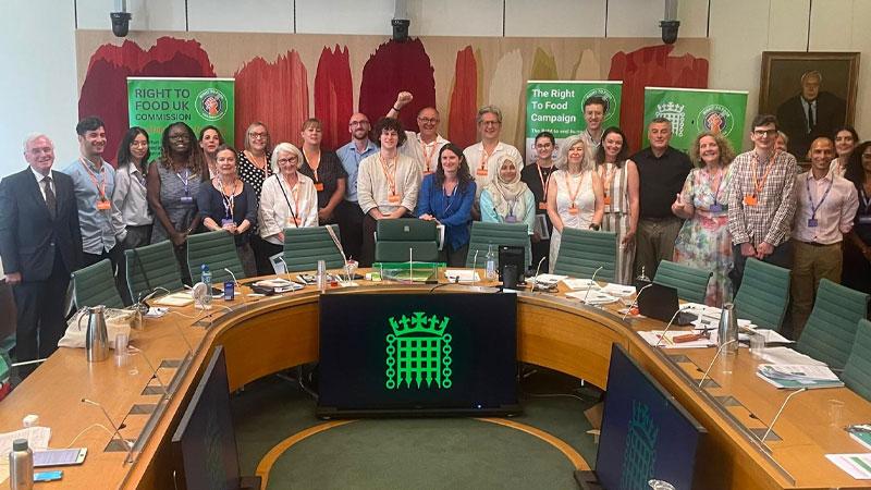 Photo of commissioners standing in parliament around a U-shaped wooden table
