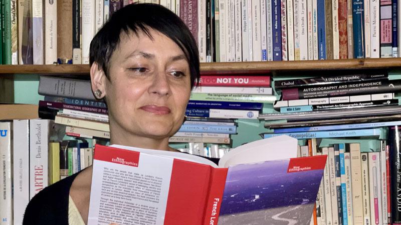 Saskia Huc-Hepher sat in front of bookshelf reading 'French London' book