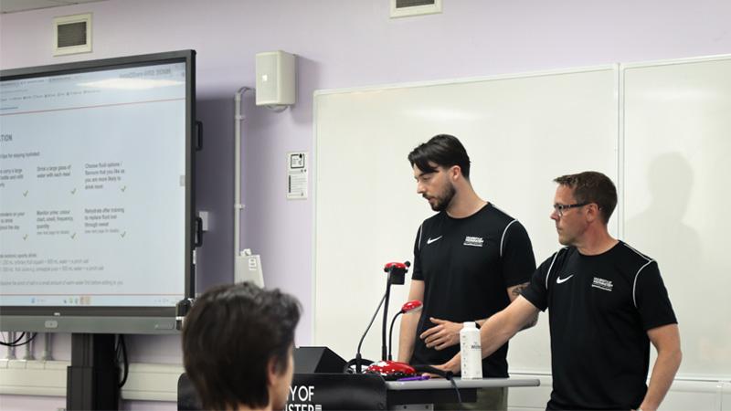 Liam Carroll and Gareth Bowen stand in front of a lectern speaking into a microphone.