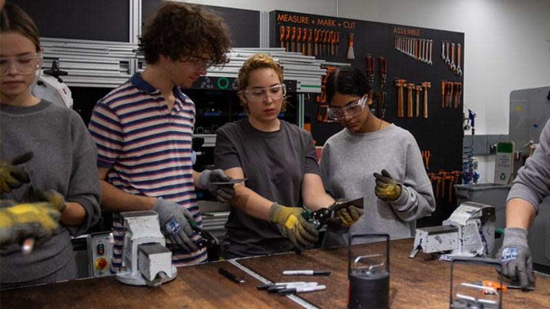 Technicians helping students with metalwork on a work top in the Fab Lab metal shop.