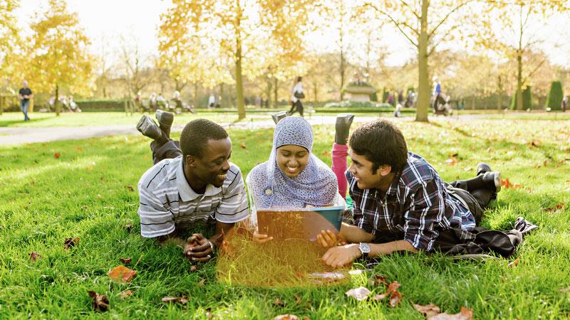 Three students in the park sat on the grass smiling