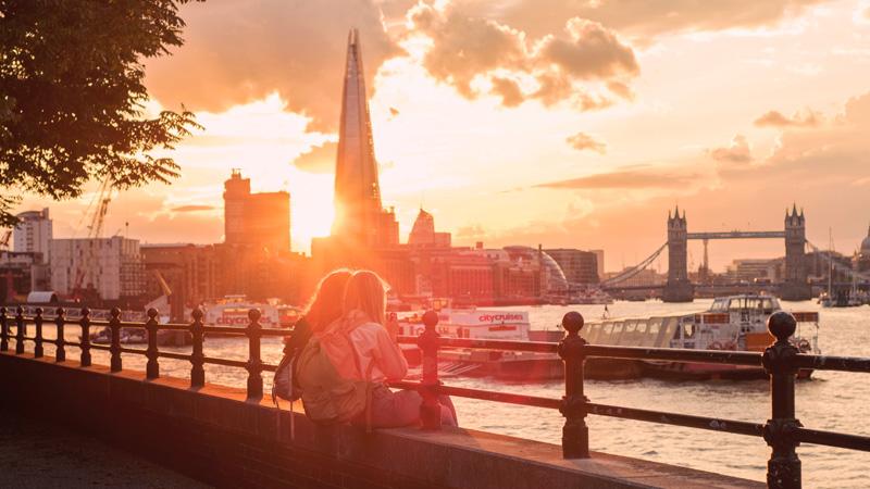 Two women sat on ledge overlooking sunset in London