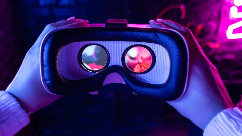 Pair of hands holding a virtual reality headset with the glare of pink-coloured neon light behind it