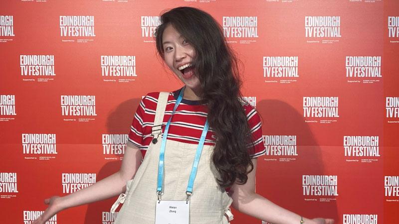 Xiaoyu Zhang in front of a red background with the Edinburgh TV Festival logo