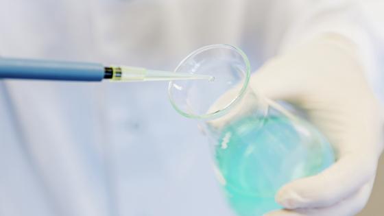 Putting blue liquid into a glass container using a syringe