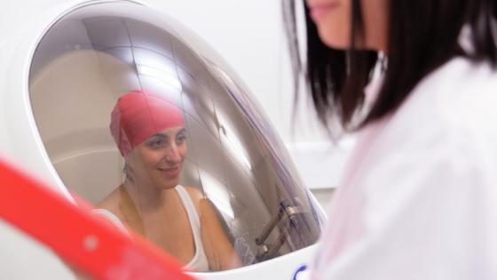 A female athlete sitting in a pod with a glass window, whilst a female in a white coat attends outside the pod