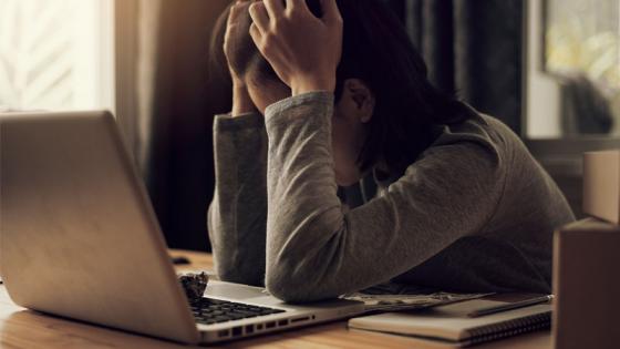 Picture of a woman at a laptop, head in hands, inferring that she is stressed