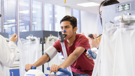 A man working out on a bicycle whilst being tested by someone in a white coat