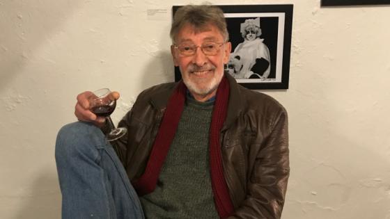 A picture of Fred sitting down with a glass of red wine in his hand and a huge smile on his face